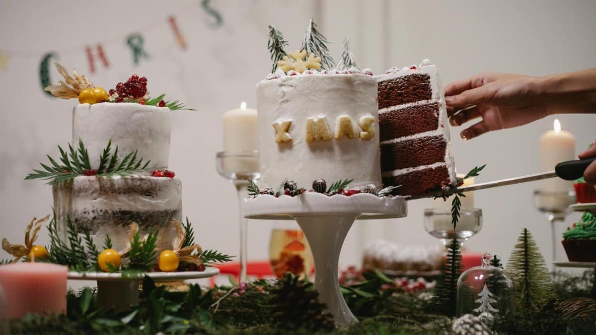 Crop anonymous cook demonstrating piece of tasty chocolate cake with Xmas inscription and rosemary decor in house