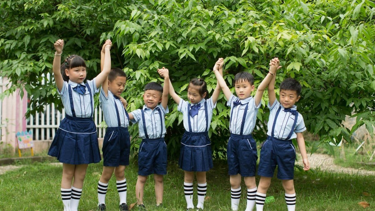 Group of Asian children in uniforms holding hands and celebrating outside.