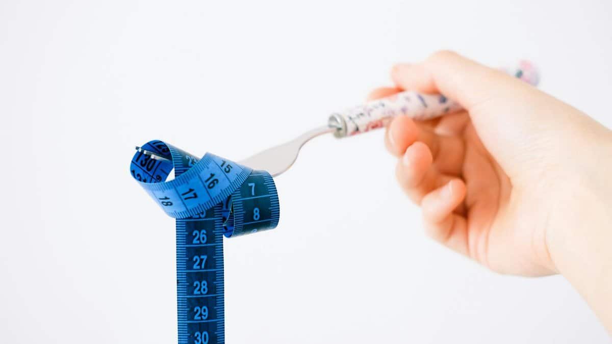 A hand holding a fork wrapped with a blue measuring tape suggesting diet or weight management.