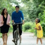 A joyful family enjoying a walk with a bicycle on a green forest path.