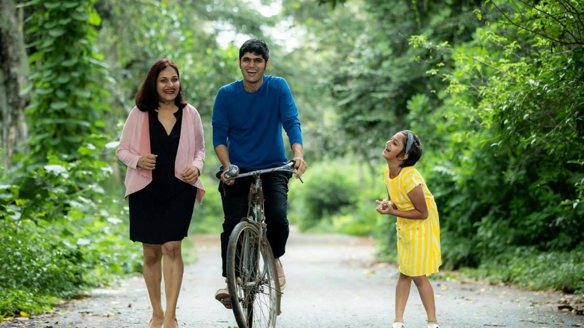 A joyful family enjoying a walk with a bicycle on a green forest path.