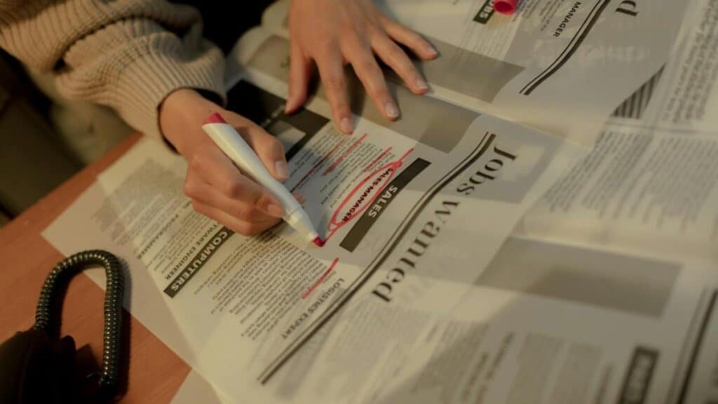 An adult woman highlights job ads in a newspaper, focusing on employment opportunities.