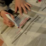 An adult woman highlights job ads in a newspaper, focusing on employment opportunities.