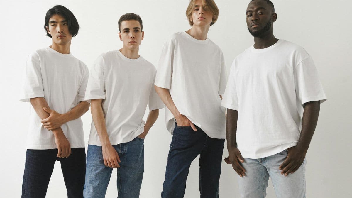 A group of four diverse men modeling white t-shirts and jeans in a studio setting.
