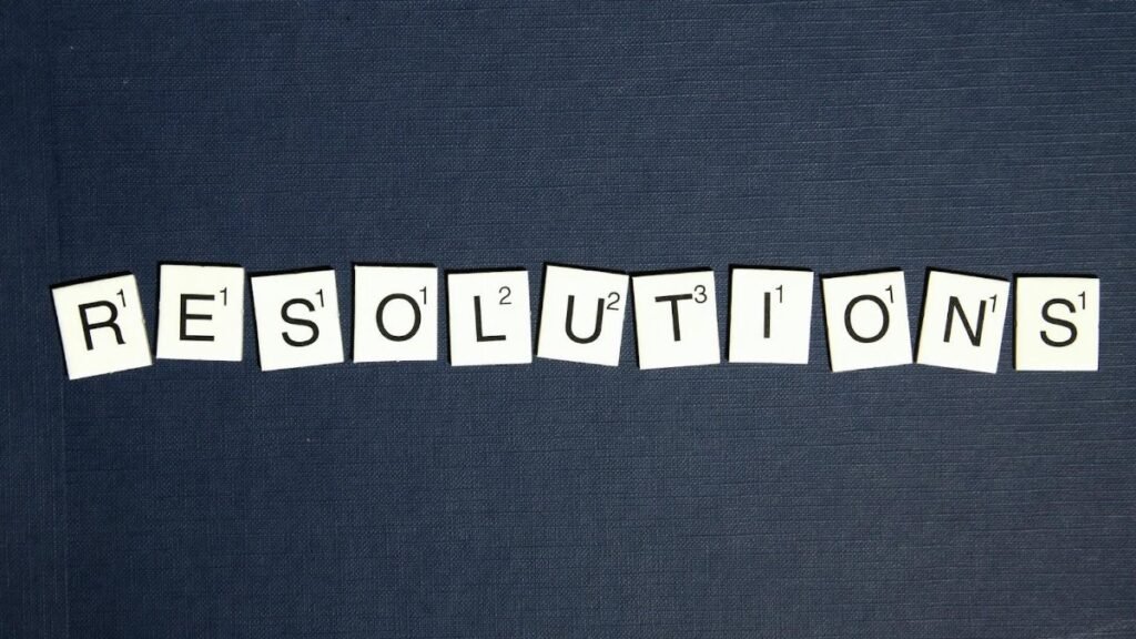 Scrabble tiles spell 'RESOLUTIONS' on a textured dark blue background, capturing a New Year theme.