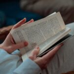 A person leisurely sitting and reading an open book indoors, capturing the essence of relaxation.