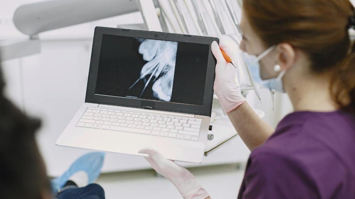 Dentist shows x-ray results on laptop to patient in dental clinic setting.