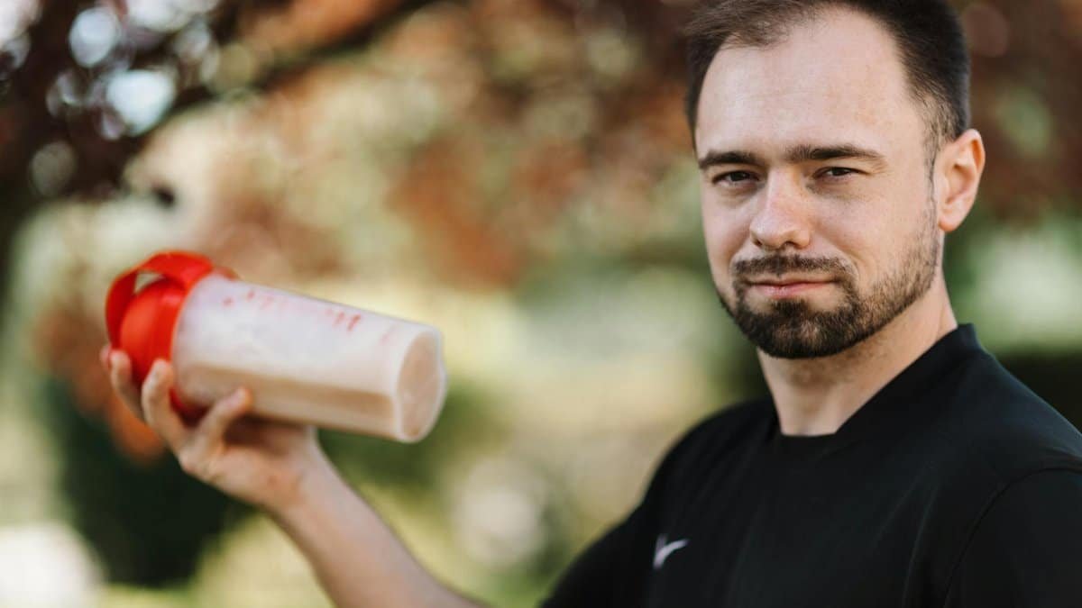 Adult man holding a protein shake outdoors during the day.