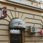 A vintage-style shopfront with multiple ABC signs and a Coca-Cola awning in an urban setting.