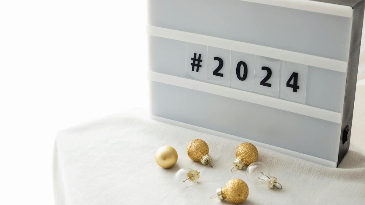 A stylish New Year 2024 decoration with gold baubles and a lightbox on a white tablecloth.