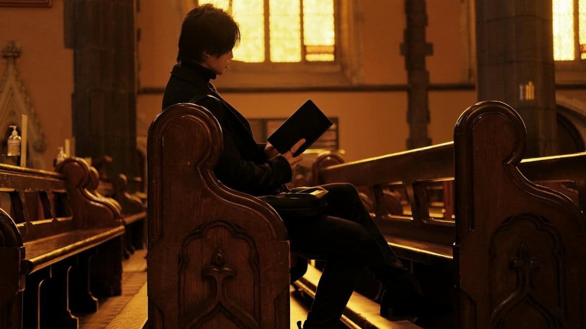 A person sits alone in a church, reading in the warm glow of stained glass windows.