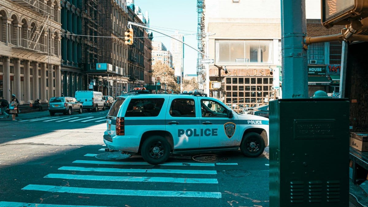 A police SUV at an urban intersection in New York City with pedestrians and traffic.