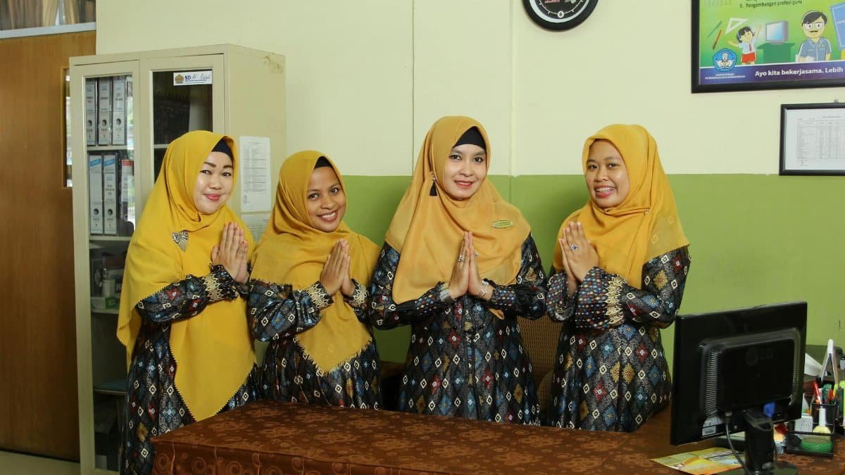 Indonesian female teachers in traditional dress standing indoors, showcasing cultural clothing.