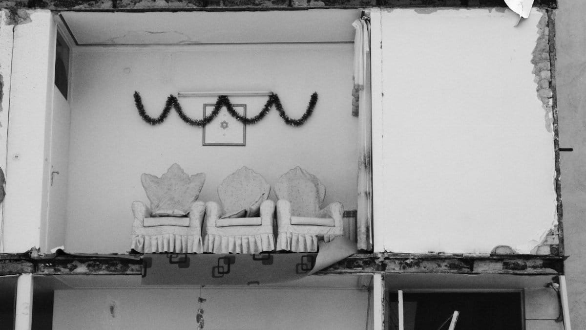 Black and white photo of a room with chairs amid building collapse.