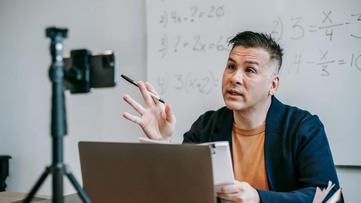 Instructor teaching math online using laptop and webcam, engaging students in a virtual classroom.