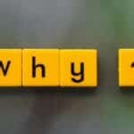 Yellow letter tiles spelling 'why?' create a thought-provoking scene on a green blurred background.