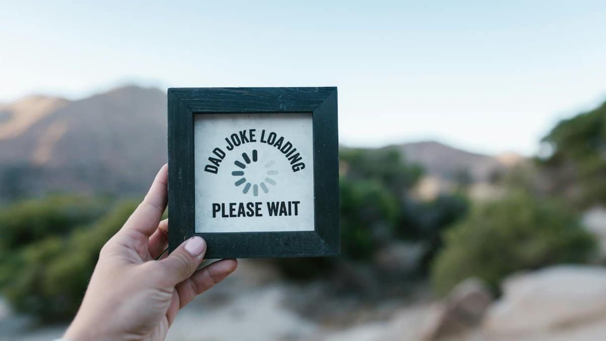 A hand holds a picture frame with 'Dad Joke Loading' text in a natural setting.