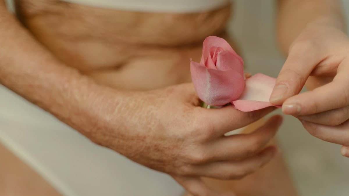 Intimate close-up of burn scarred hands gently holding a pink rose, focusing on healing and beauty.