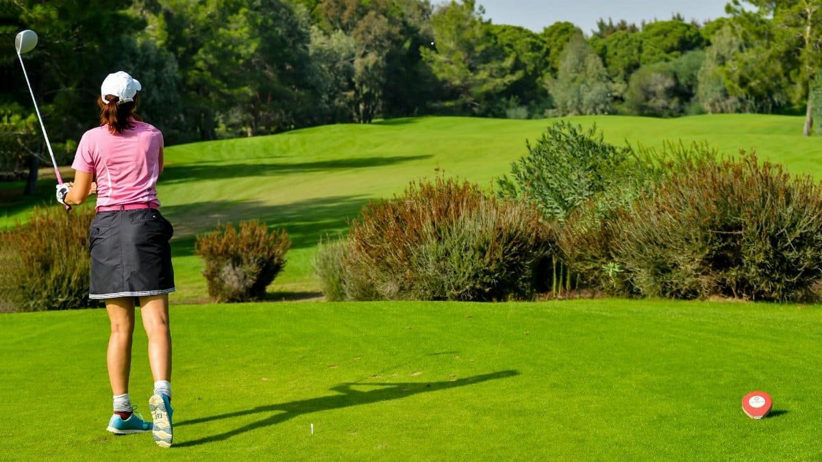 Woman playing golf on a vibrant green course with scenic tree backdrop.