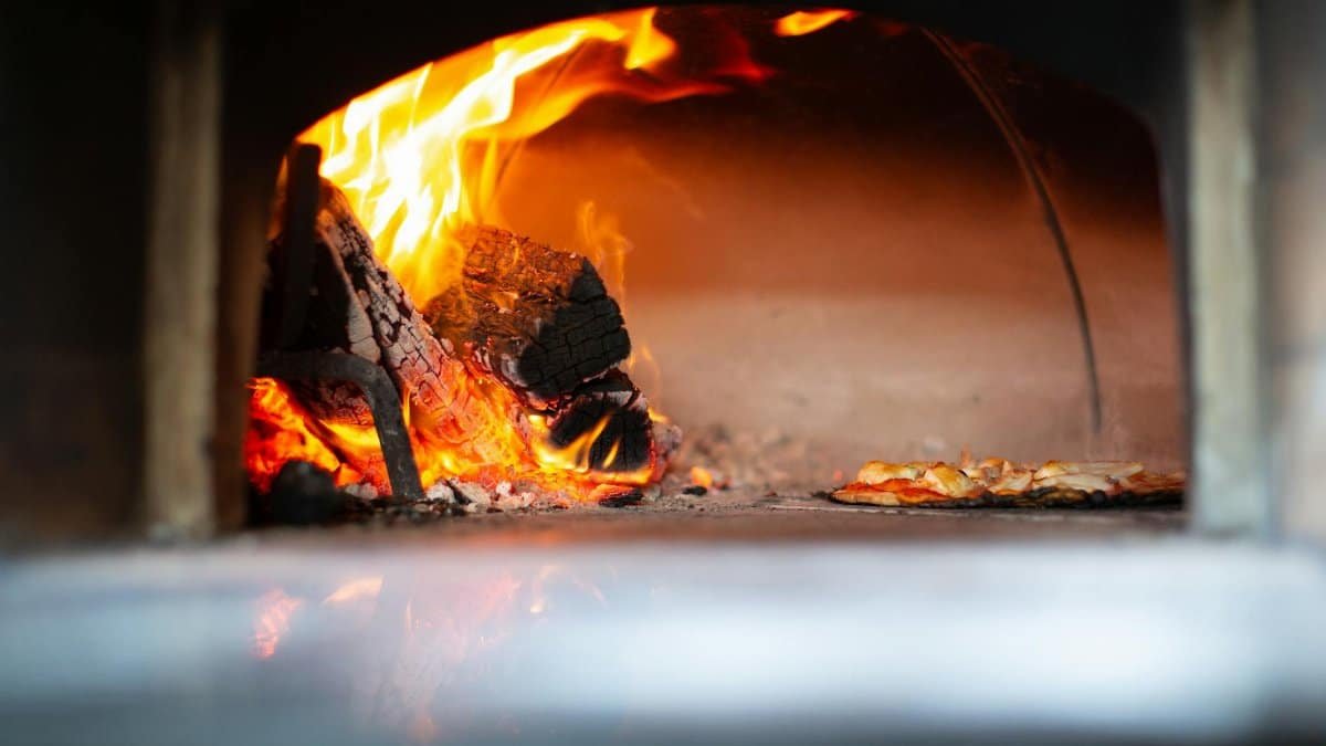 Authentic pizza baking with open flames in a traditional wood-fired oven, creating a rustic gourmet experience.