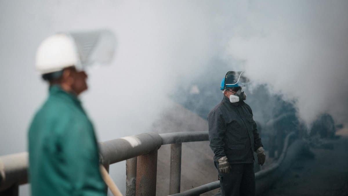 Industrial workers wearing safety gear amidst heavy smoke, illustrating pollution and safety measures.