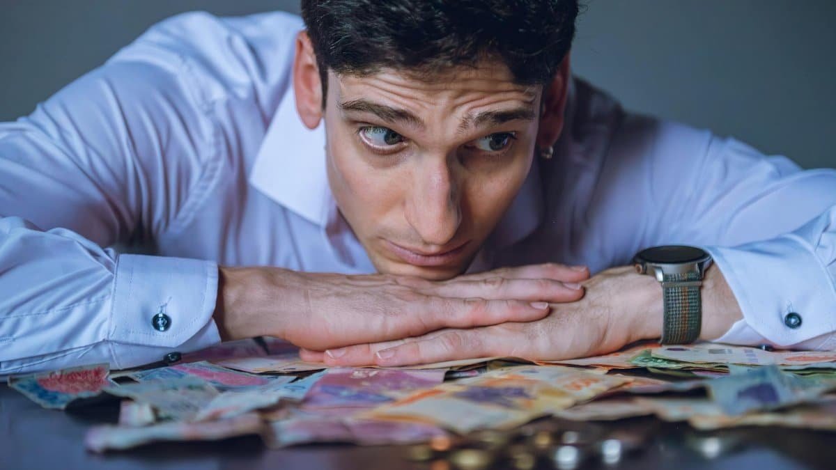 Young man in white shirt pondering over Argentine bills, symbolizing financial uncertainty.