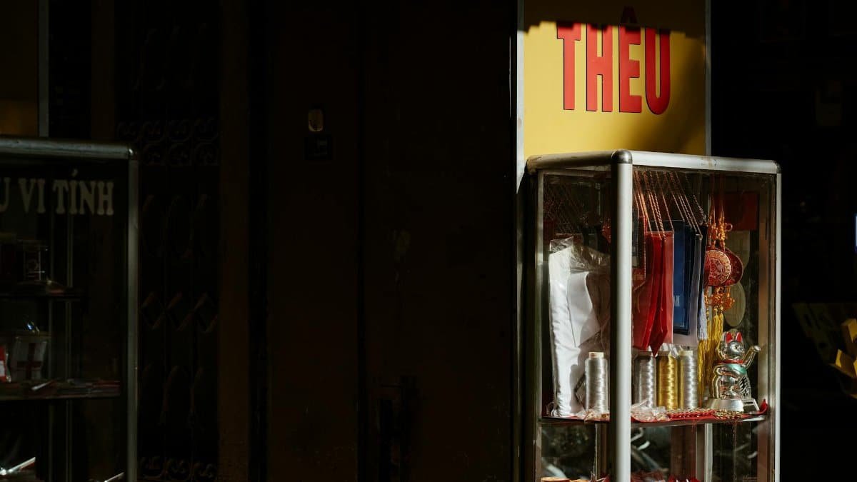 Glass cabinet in store with sunlight on Asian souvenirs including lucky cat and thread.