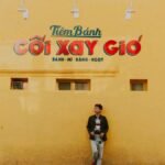 A man stands against a vibrant yellow wall in Vietnam, capturing the urban essence.