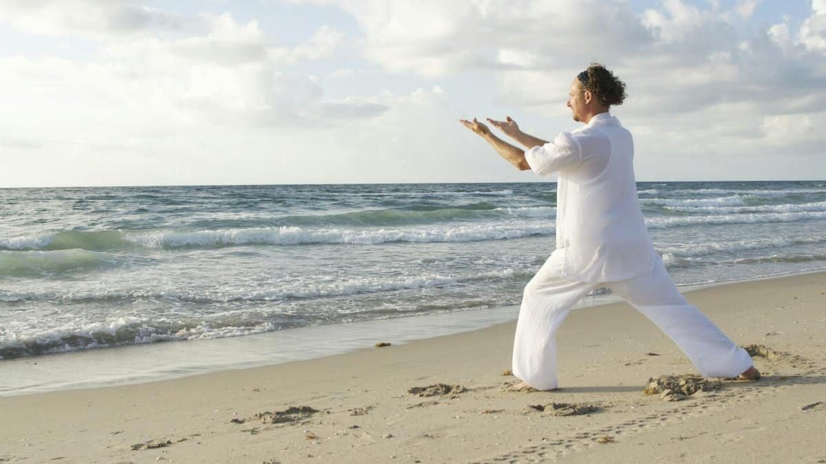 A serene scene of a man practicing Tai Chi on a quiet beach with gentle waves.