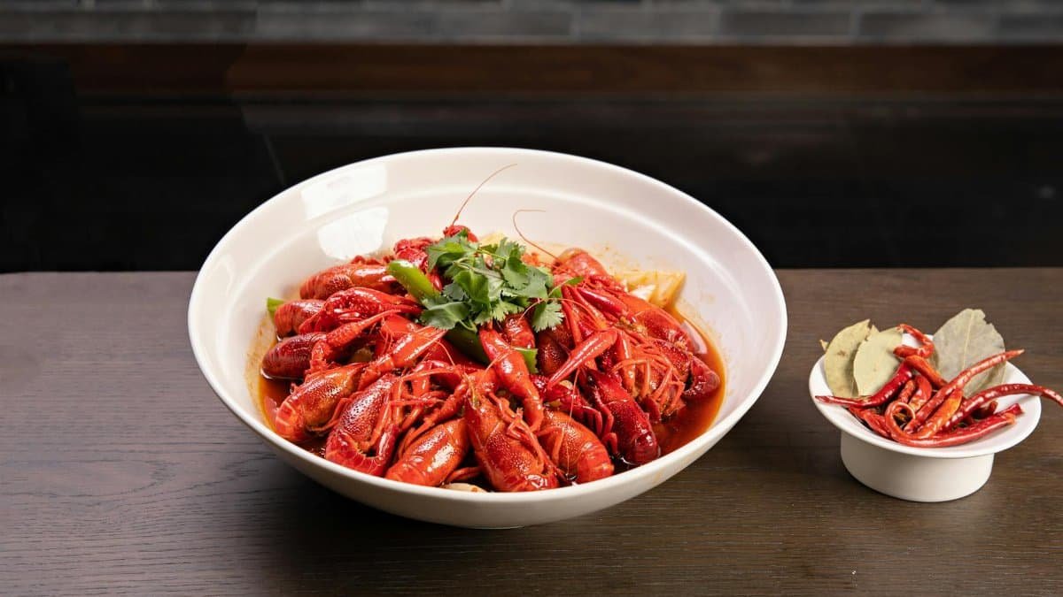 A bowl of spicy boiled crawfish garnished with herbs, served with chili and bay leaves.