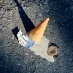 A dropped ice cream cone melting on the asphalt with a parking ticket nearby.