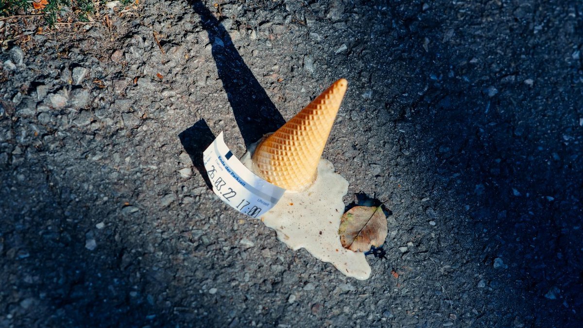 A dropped ice cream cone melting on the asphalt with a parking ticket nearby.