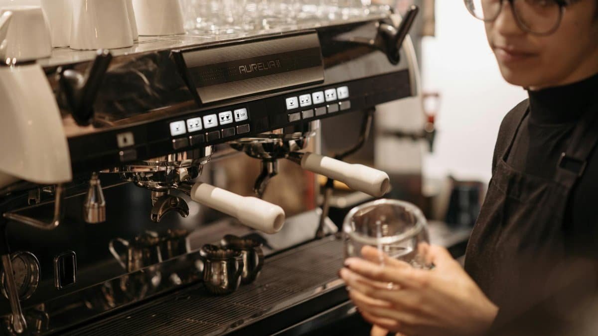 Barista in black apron making coffee with espresso machine at a cozy cafe.