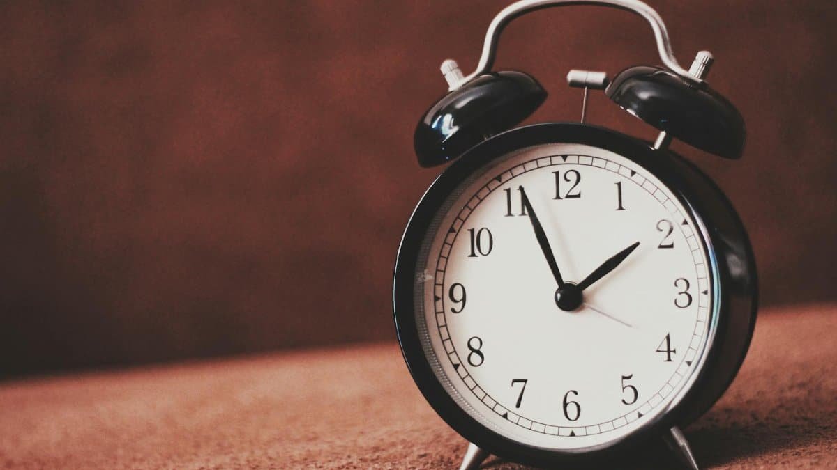 Close-up of a vintage black alarm clock showing twelve o'clock against a brown backdrop.