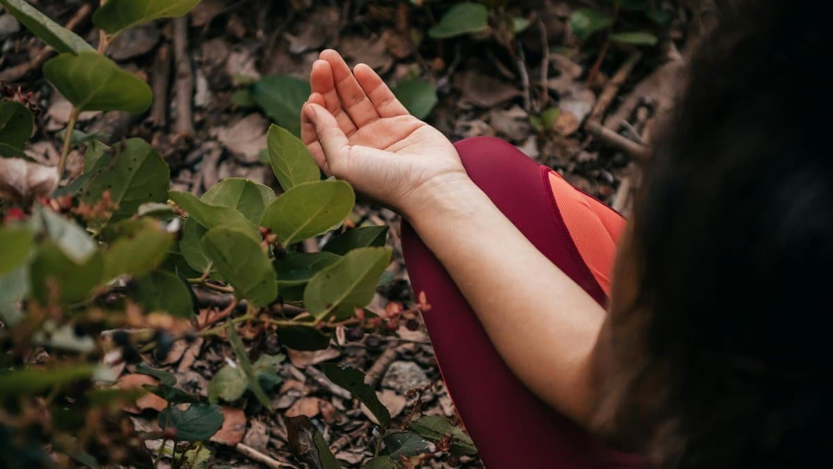 Close-up of a person meditating outdoors surrounded by green leaves, promoting relaxation and mental health.