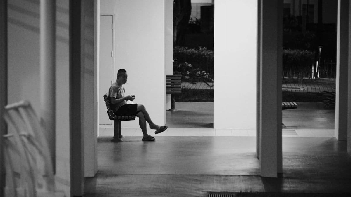Dramatic black and white photo of a person sitting alone on a bench in an urban setting at night.