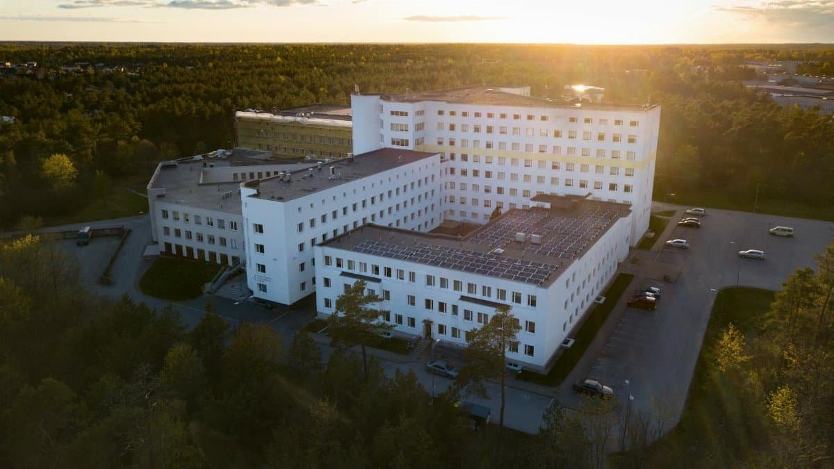 Aerial view of a modern hospital building surrounded by greenery at sunset, illustrating serene healthcare environment.
