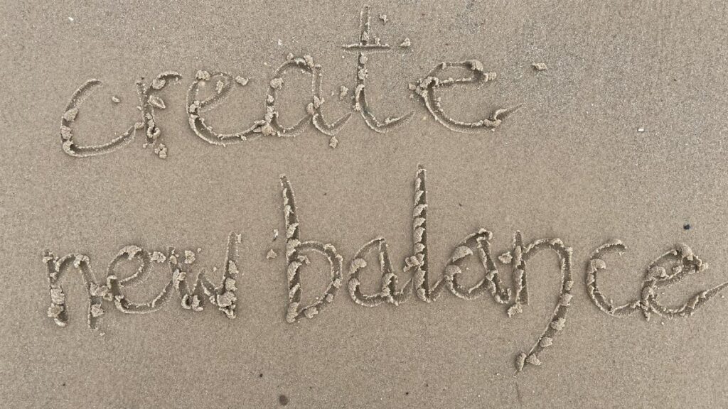 Sand writing 'create new balance' on a Scottish beach, symbolizing fresh starts and harmony.