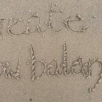 Sand writing 'create new balance' on a Scottish beach, symbolizing fresh starts and harmony.