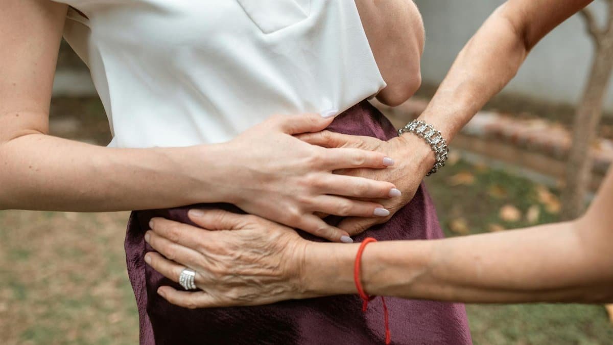 A close-up of multiple hands supporting a pregnant woman outdoors, symbolizing care and support.