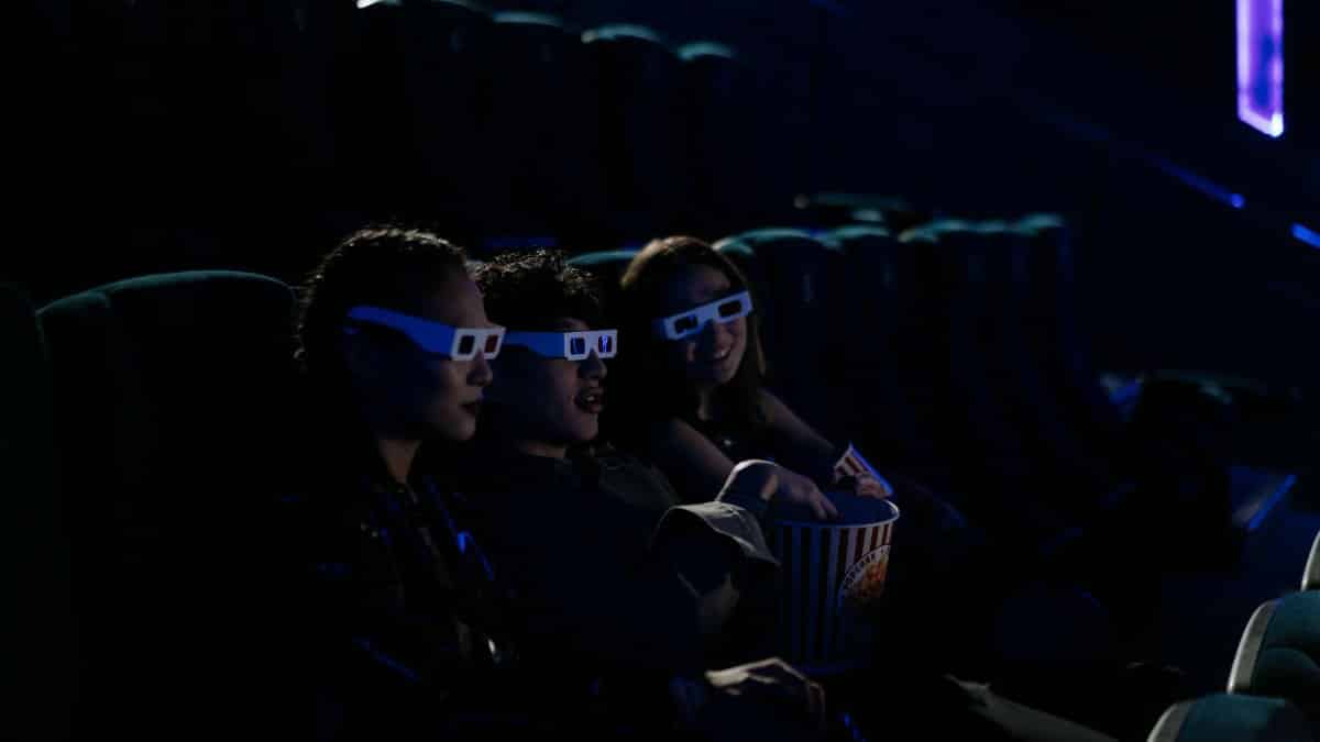 Group of friends wearing 3D glasses enjoying a film at a cinema with popcorn.