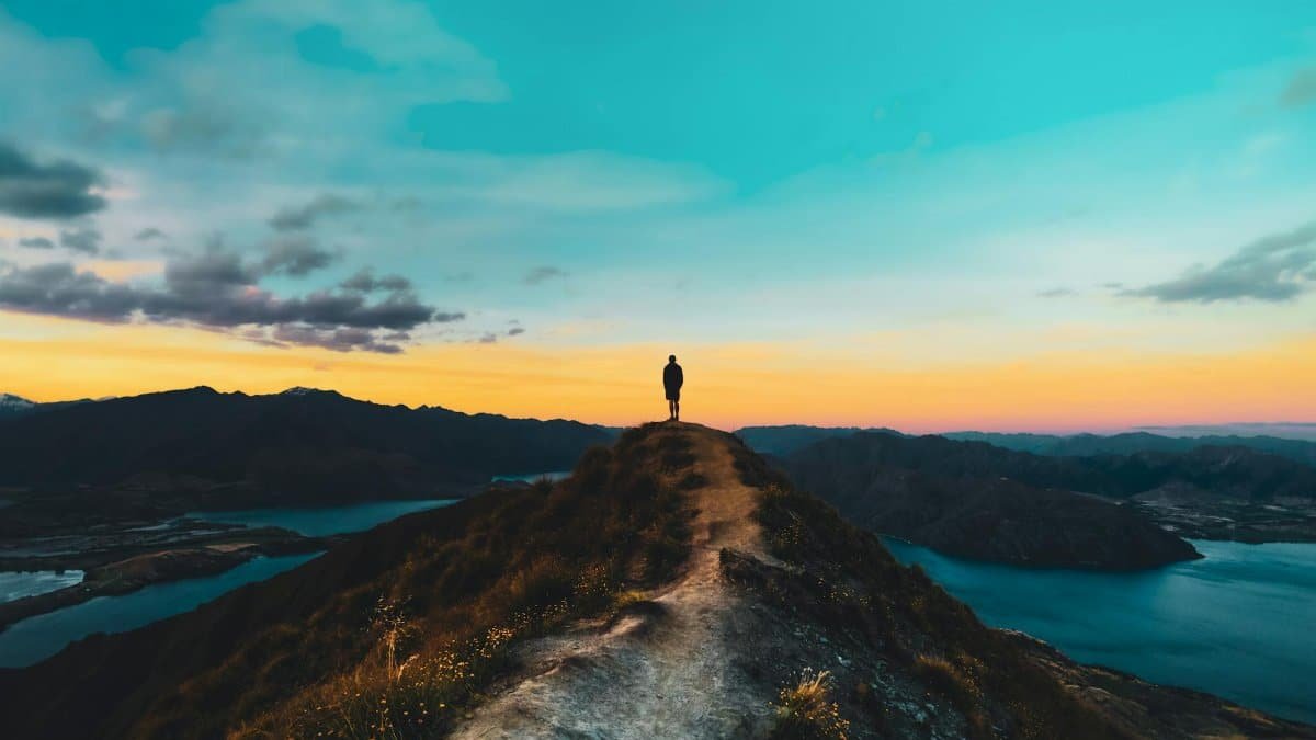 Person silhouetted on Roys Peak with breathtaking sunset view, Wanaka, New Zealand.