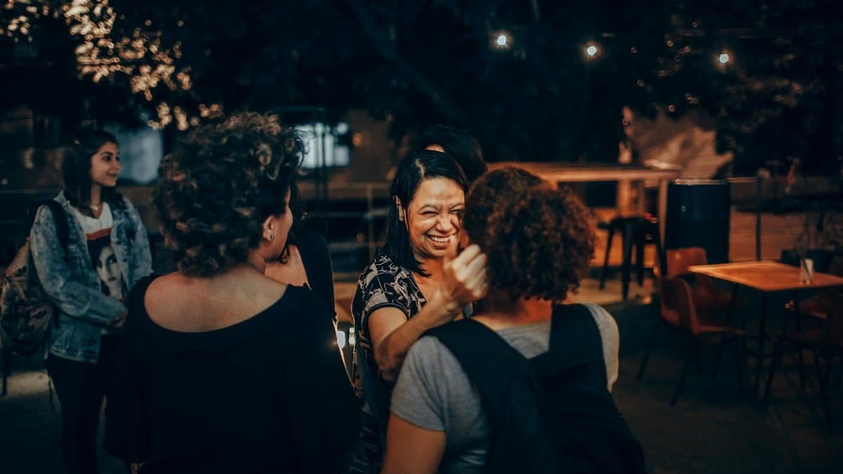 Friends enjoying a night out in a cozy outdoor cafe, sharing laughter and conversation under warm lights.