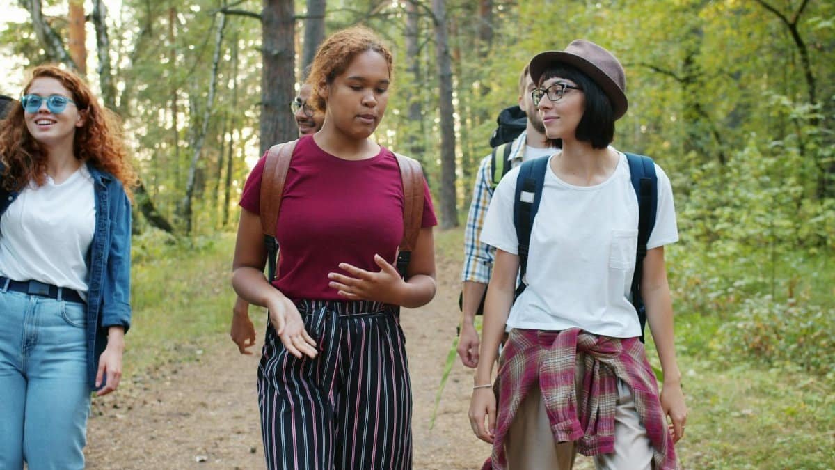 A diverse group of young adults hiking through a lush forest, enjoying their outdoor adventure.