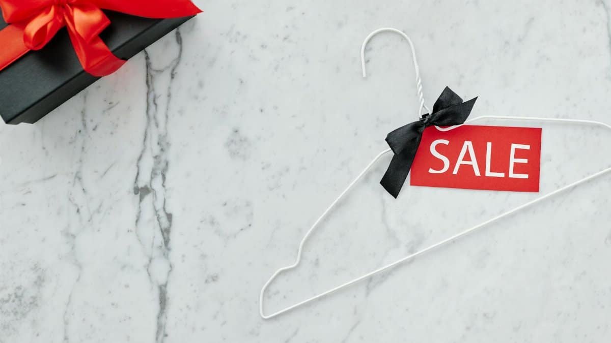 Flat lay of a sale tag on a hanger and gift box on marble, perfect for holiday promotions.