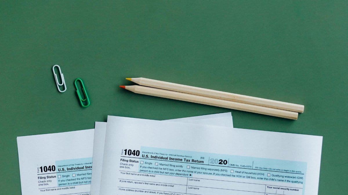 U.S. tax forms with pencils and paperclips on green surface in a flat lay setup.