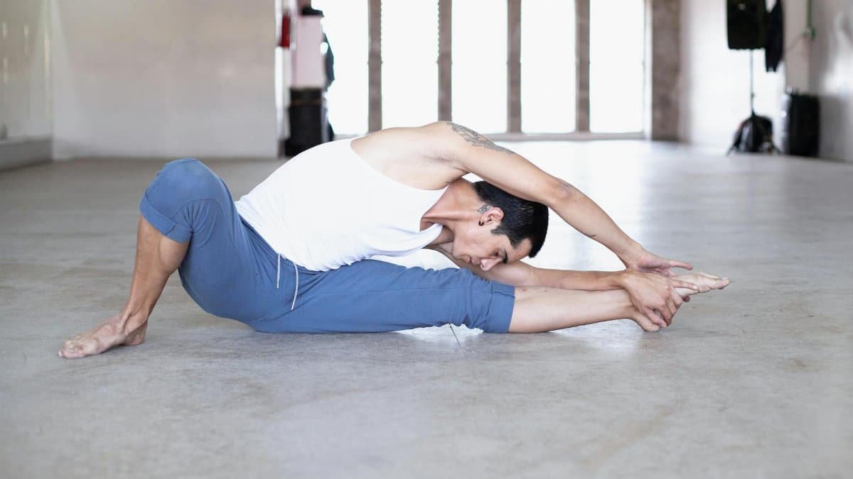 Male ballet dancer stretching during practice in a bright dance studio.