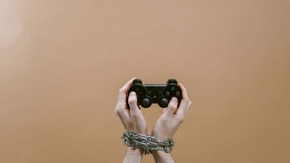 Conceptual image of hands in chains holding a game controller symbolizing gaming addiction.