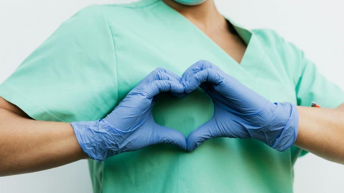 Nurse in blue gloves making a heart shape with hands, symbolizing compassion and care.