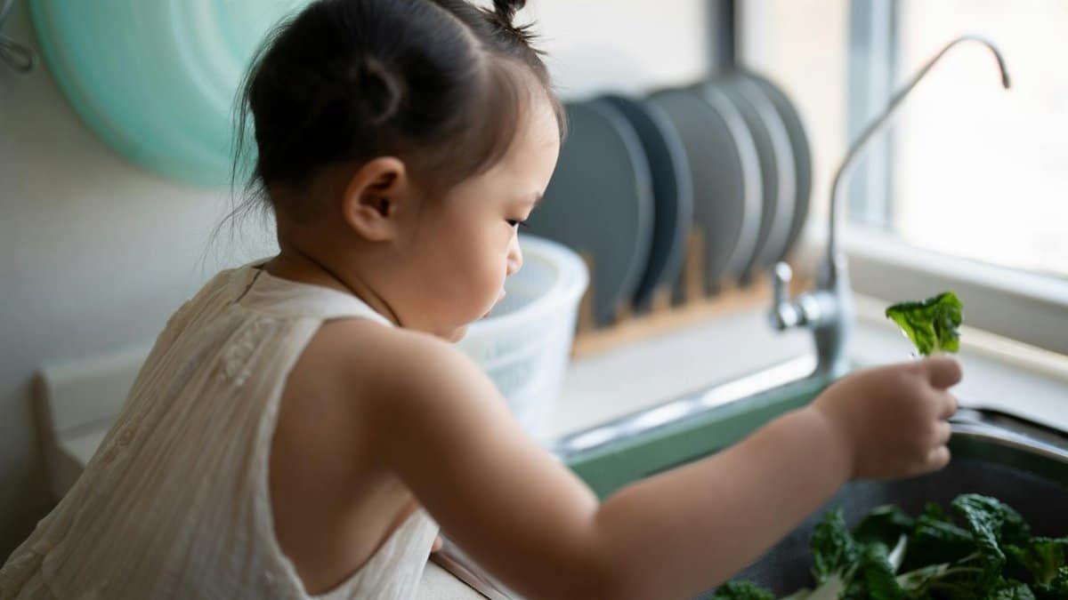 A child washing fresh vegetables at the sink, demonstrating healthy habits.